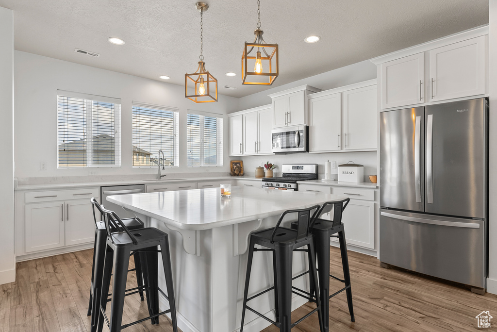 Kitchen with decorative light fixtures, appliances with stainless steel finishes, a center island, and hardwood / wood-style flooring