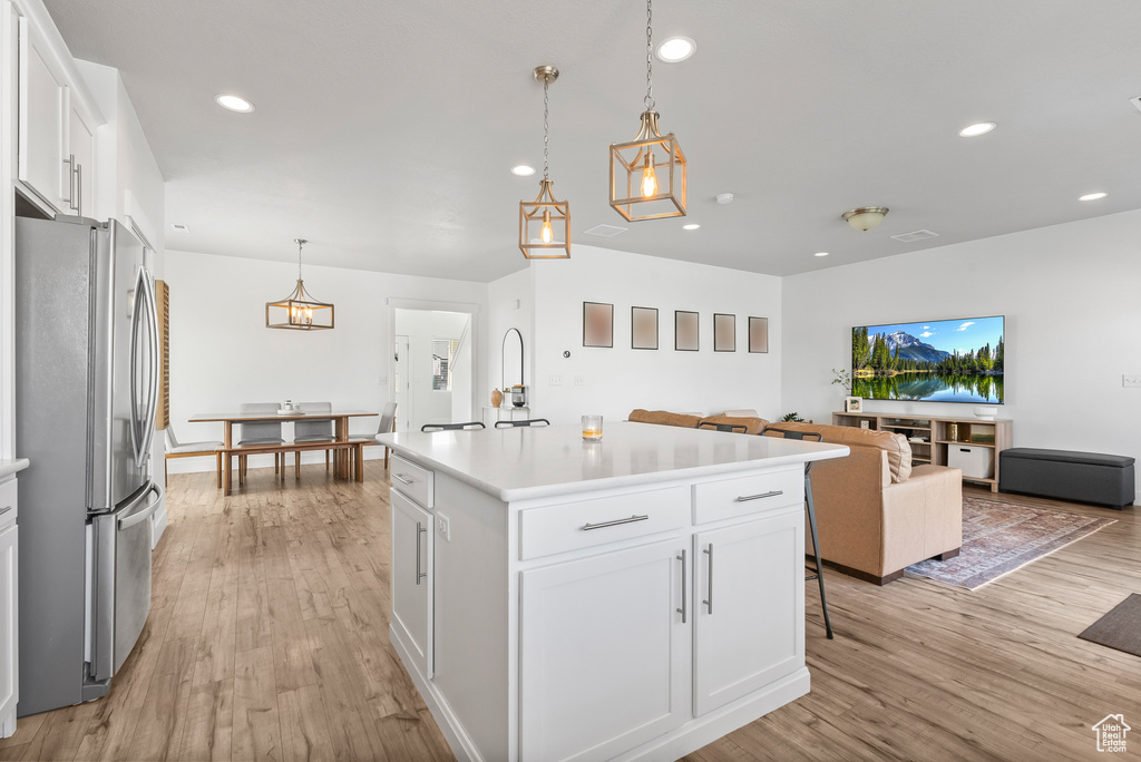 Kitchen with a kitchen island with sink, white cabinets, light wood-type flooring, stainless steel fridge, and pendant lighting