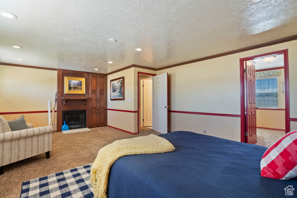 Bedroom with crown molding, a fireplace, carpet floors, and a textured ceiling