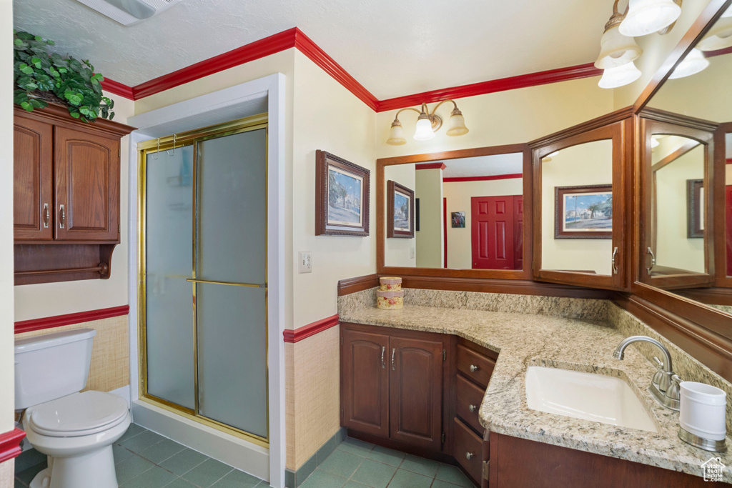 Bathroom with tile flooring, vanity with extensive cabinet space, crown molding, toilet, and a shower with shower door
