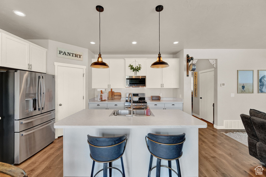 Kitchen with pendant lighting, stainless steel appliances, a center island with sink, and light wood-type flooring