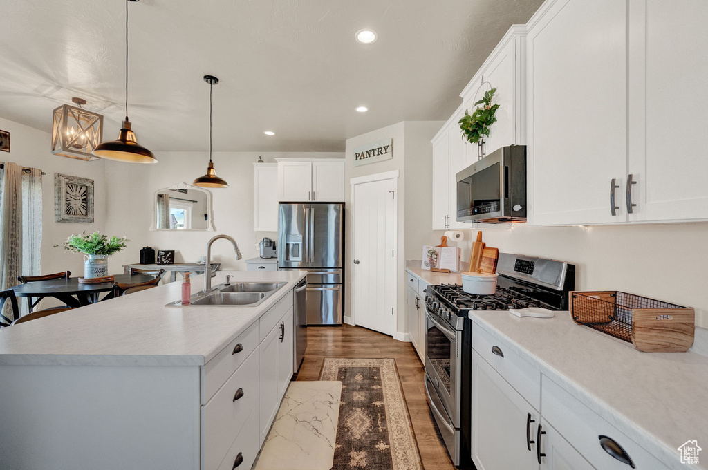Kitchen with appliances with stainless steel finishes, hanging light fixtures, a center island with sink, white cabinetry, and hardwood / wood-style floors