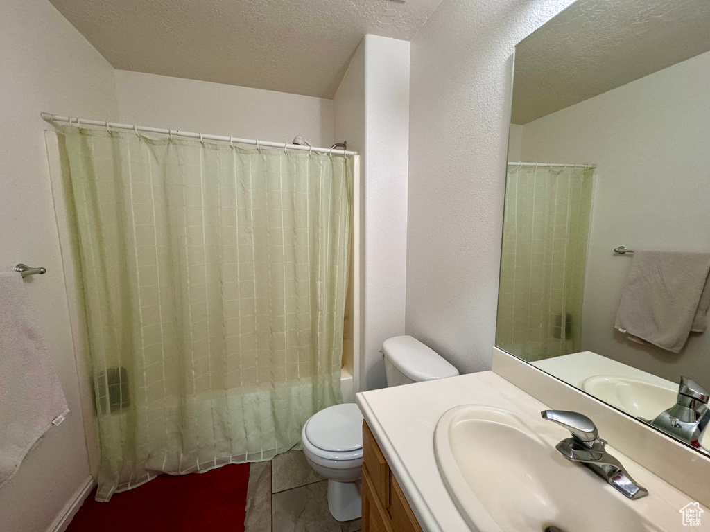 Full bathroom featuring shower / bath combo, vanity, tile flooring, toilet, and a textured ceiling