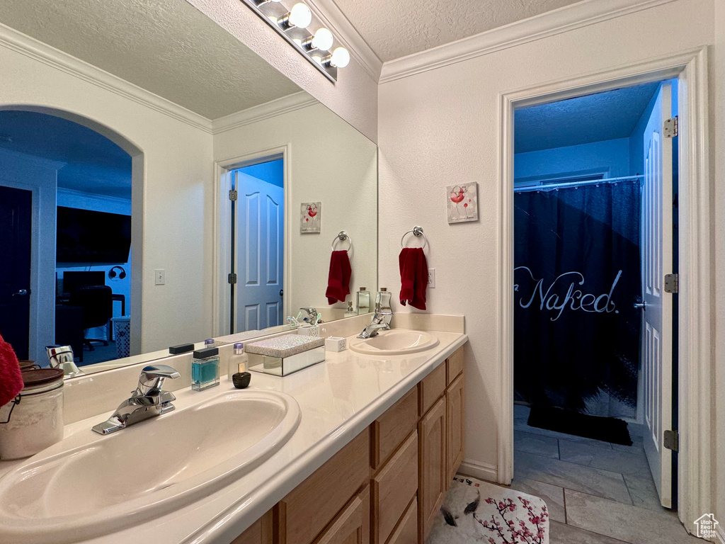 Bathroom featuring a textured ceiling, ornamental molding, dual vanity, and tile flooring