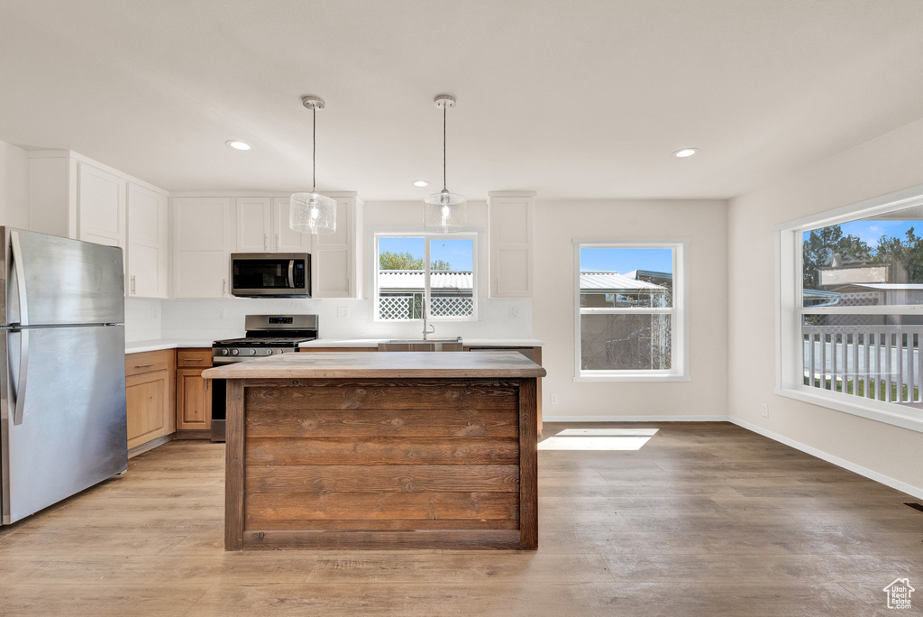 Kitchen with a center island, sink, light wood-type flooring, decorative light fixtures, and stainless steel appliances