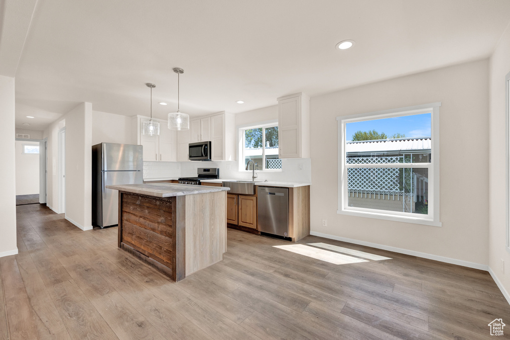 Kitchen featuring pendant lighting, appliances with stainless steel finishes, sink, a kitchen island, and light hardwood / wood-style floors