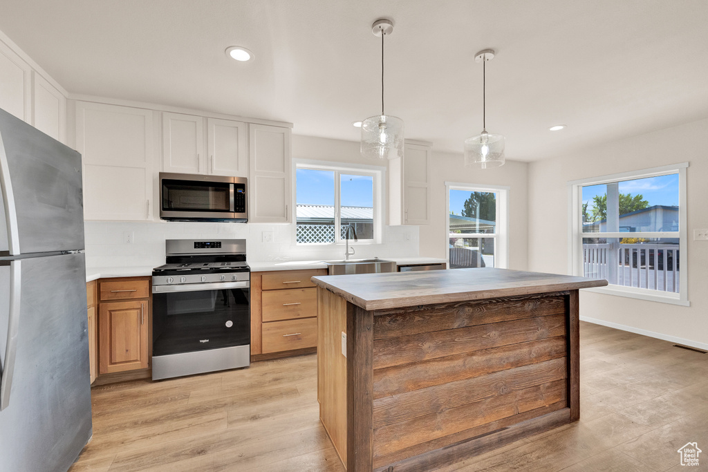 Kitchen with appliances with stainless steel finishes, a kitchen island, white cabinets, backsplash, and light wood-type flooring
