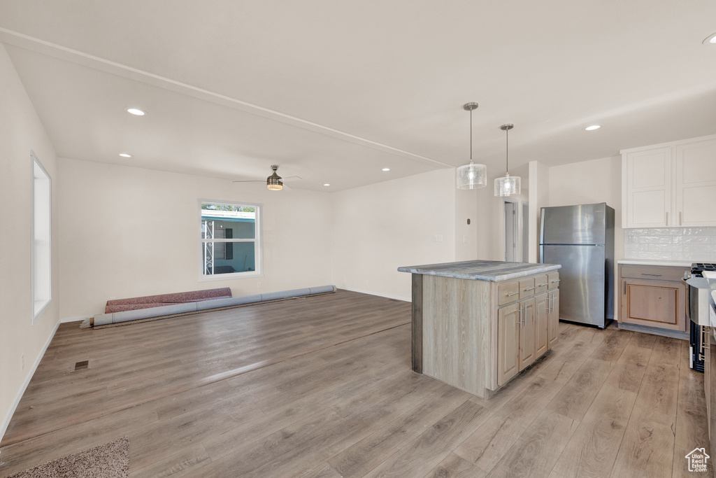 Kitchen featuring a center island, light wood-type flooring, backsplash, stainless steel fridge, and ceiling fan