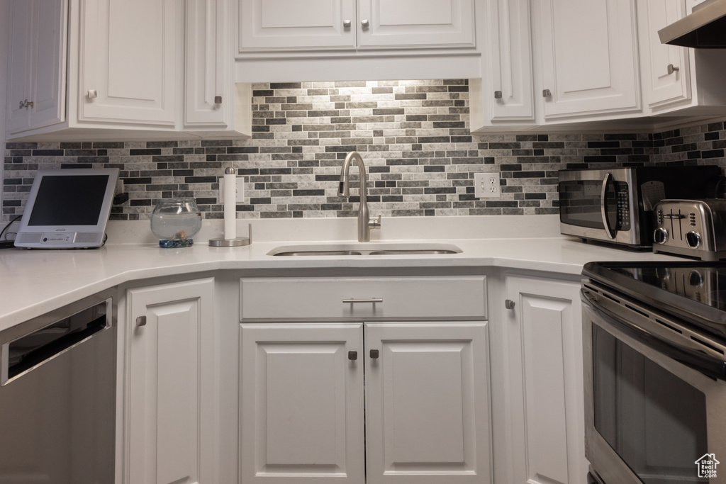 Kitchen featuring backsplash, stainless steel appliances, white cabinets, and sink
