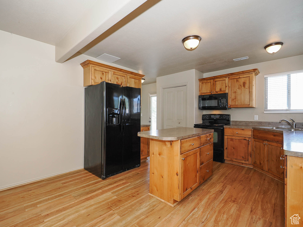 Kitchen with a kitchen island, light hardwood / wood-style floors, black appliances, and sink