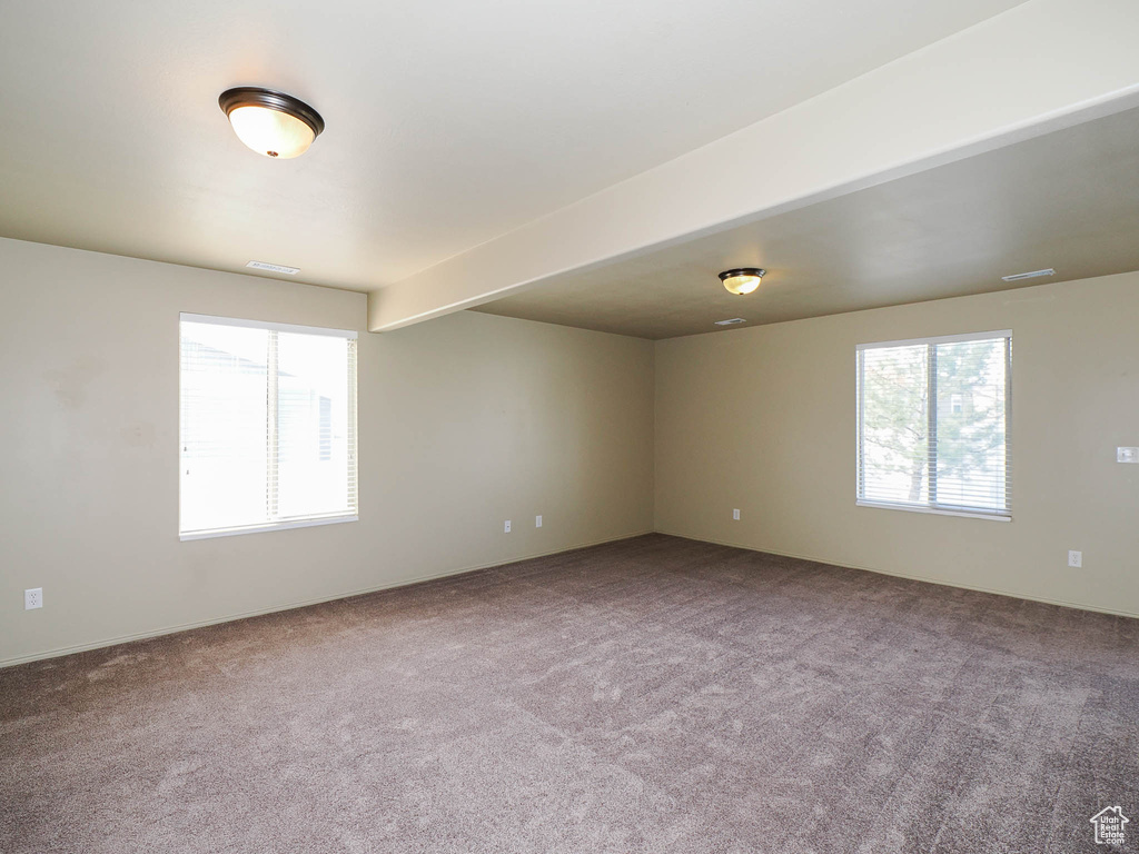Carpeted spare room with plenty of natural light and beam ceiling