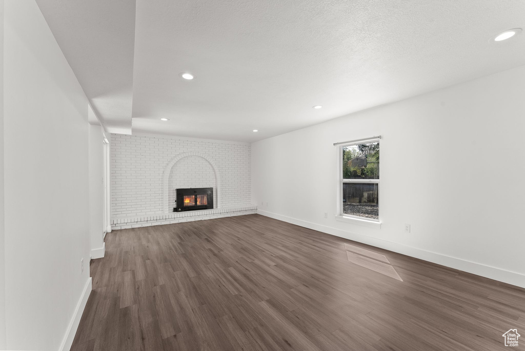 Unfurnished living room featuring dark hardwood / wood-style floors and a brick fireplace