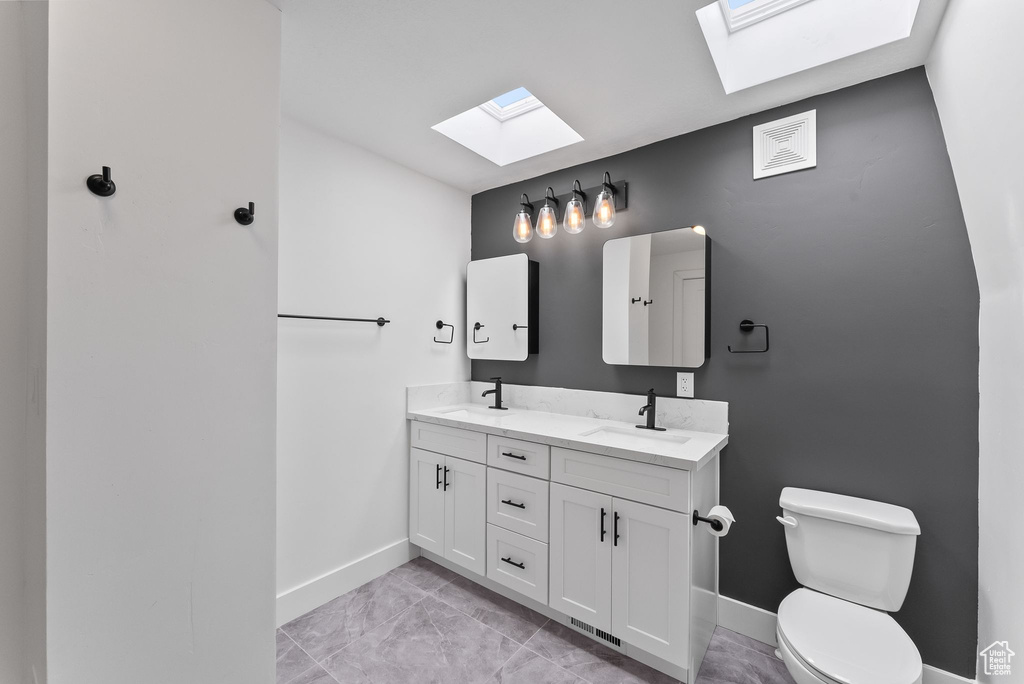 Bathroom featuring a skylight, toilet, double vanity, and tile flooring