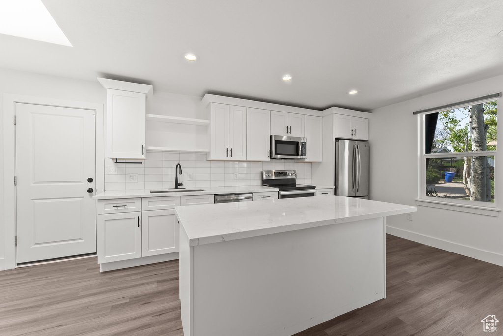 Kitchen featuring appliances with stainless steel finishes, a center island, sink, white cabinetry, and hardwood / wood-style flooring