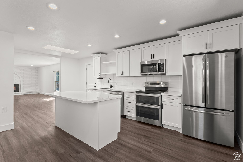 Kitchen with sink, tasteful backsplash, white cabinetry, dark wood-type flooring, and stainless steel appliances