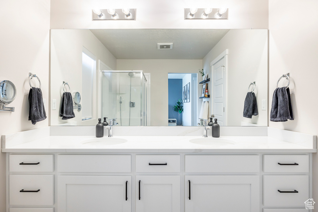Bathroom with vanity with extensive cabinet space, dual sinks, and a shower with shower door