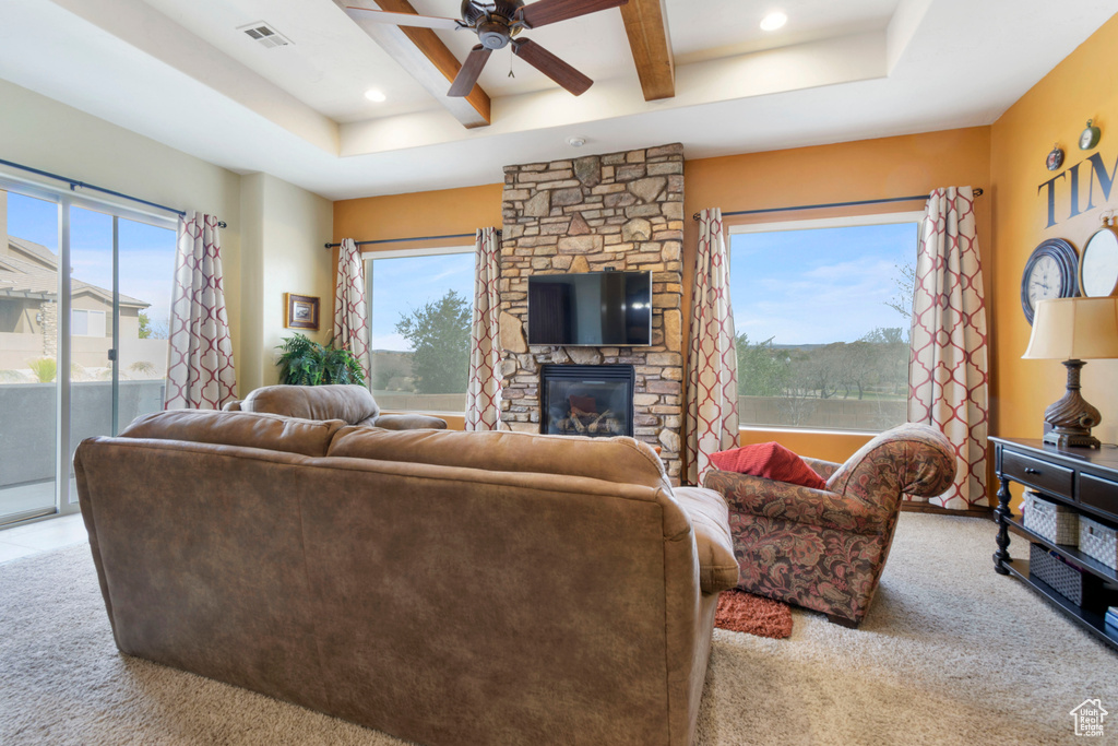 Living room featuring plenty of natural light, beam ceiling, ceiling fan, and a stone fireplace