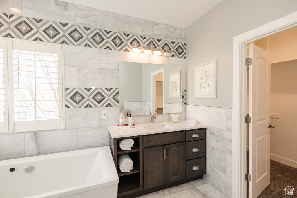 Bathroom with vanity, tile floors, tile walls, and a tub