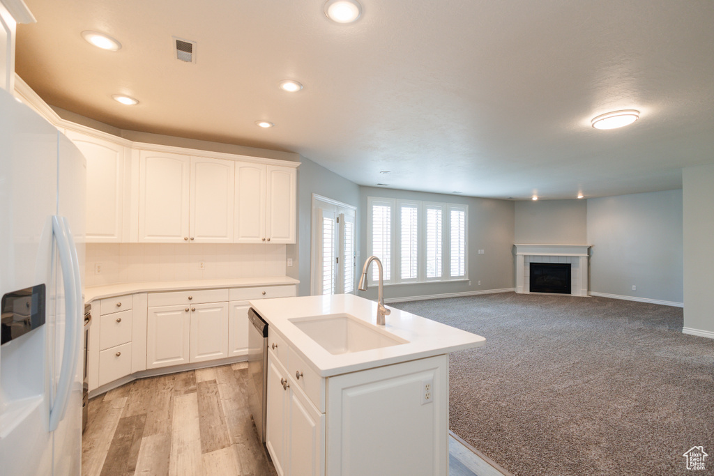 Kitchen featuring white refrigerator with ice dispenser, a tile fireplace, light carpet, white cabinetry, and sink