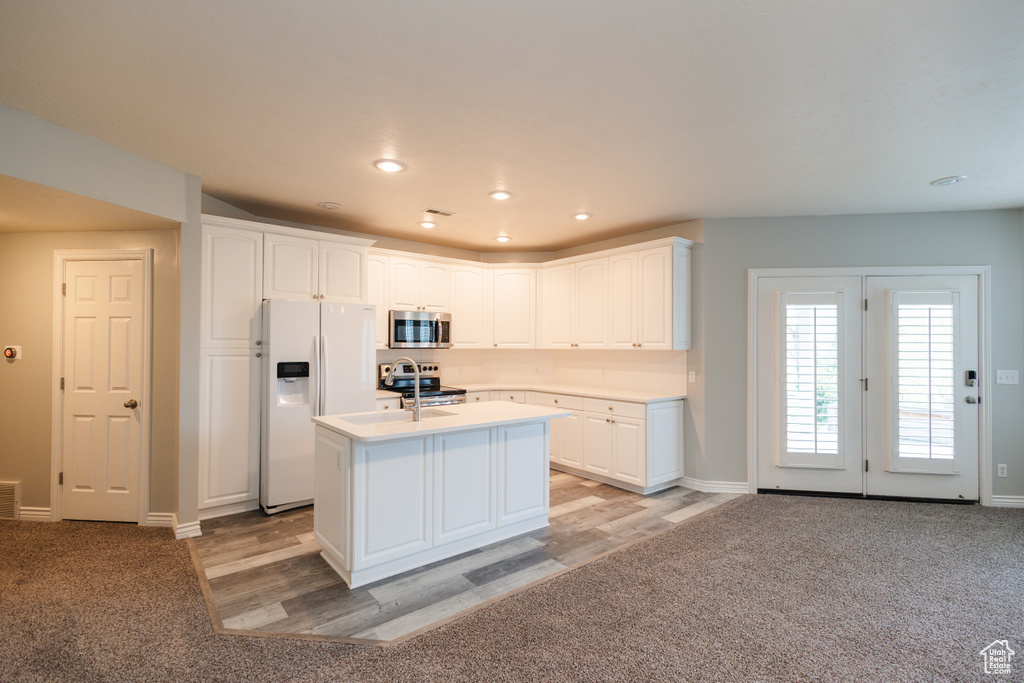 Kitchen featuring white cabinets, stainless steel appliances, light carpet, and a center island with sink