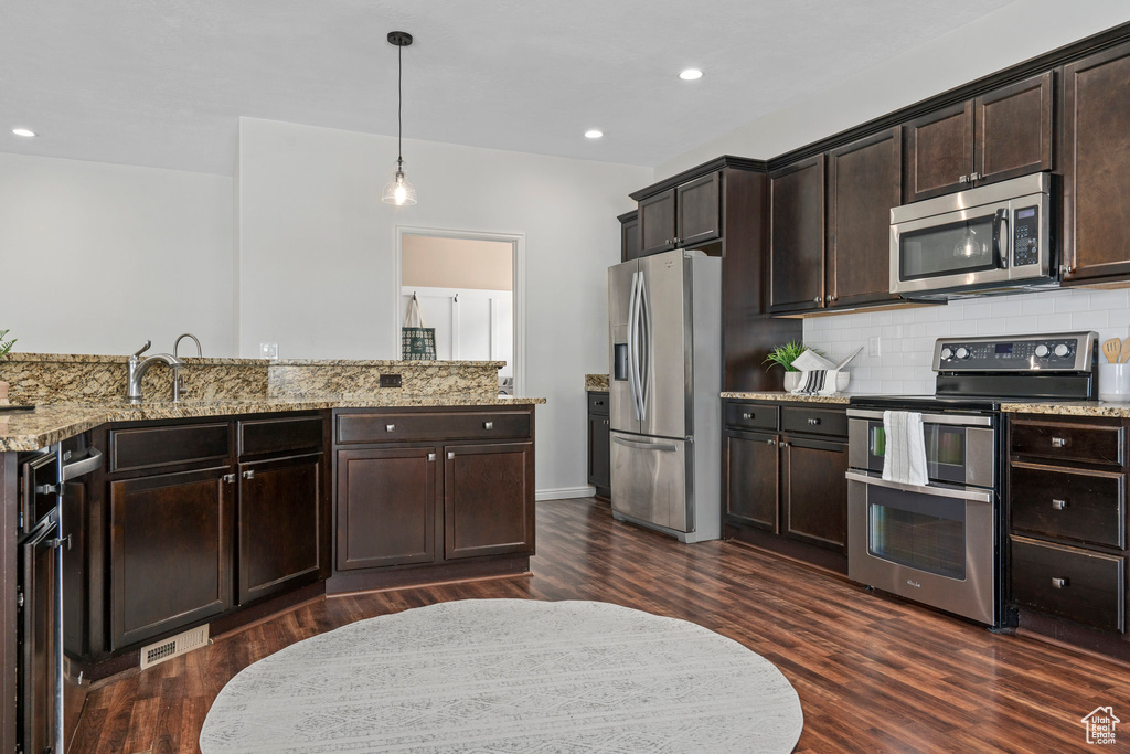 Kitchen featuring appliances with stainless steel finishes, backsplash, dark brown cabinets, dark hardwood / wood-style flooring, and light stone countertops