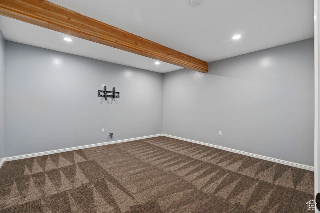 Spare room featuring dark colored carpet and beam ceiling