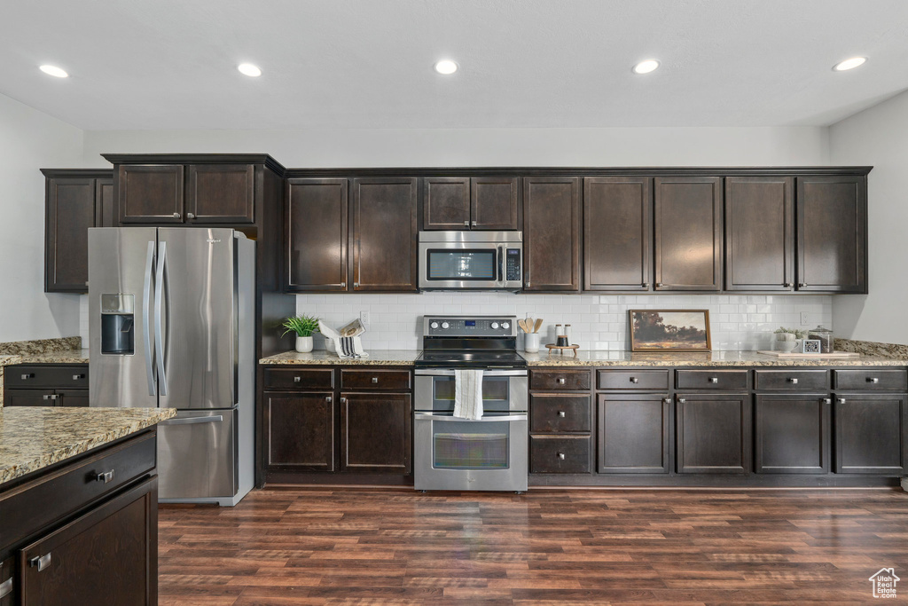 Kitchen featuring light stone counters, appliances with stainless steel finishes, tasteful backsplash, and dark hardwood / wood-style floors