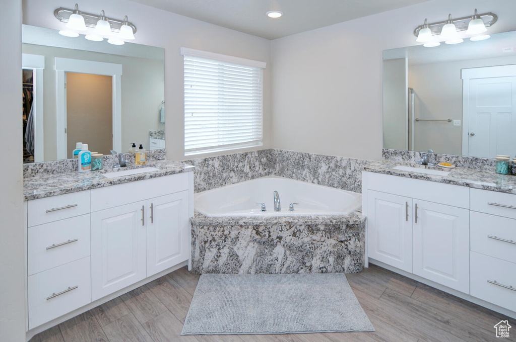 Bathroom featuring hardwood / wood-style floors, dual sinks, a relaxing tiled bath, and large vanity