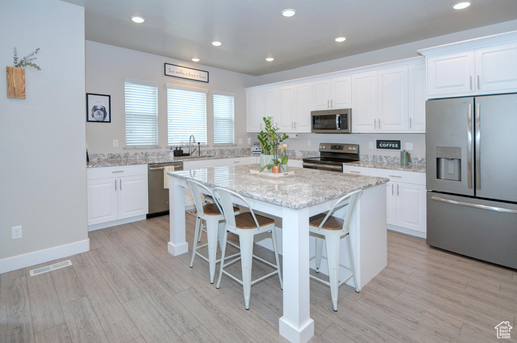 Kitchen with a center island, a kitchen breakfast bar, white cabinets, stainless steel appliances, and sink