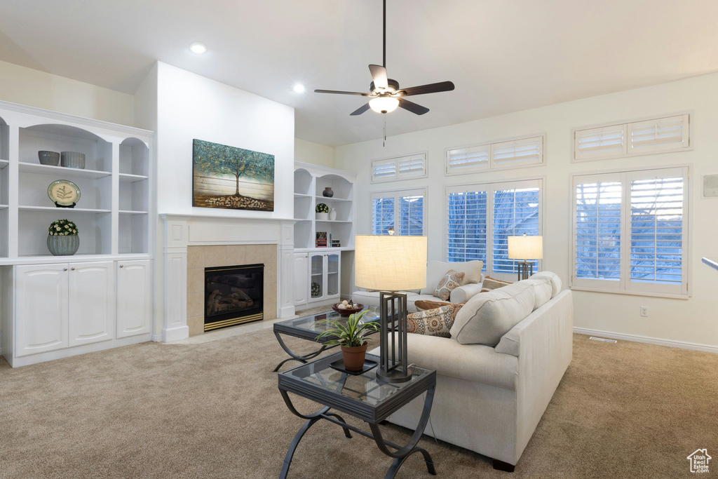Living room featuring light carpet, built in features, ceiling fan, and a tiled fireplace