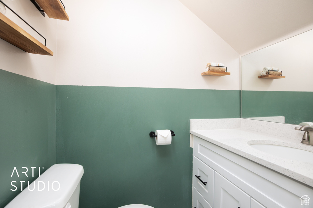 Bathroom with vaulted ceiling, vanity with extensive cabinet space, and toilet