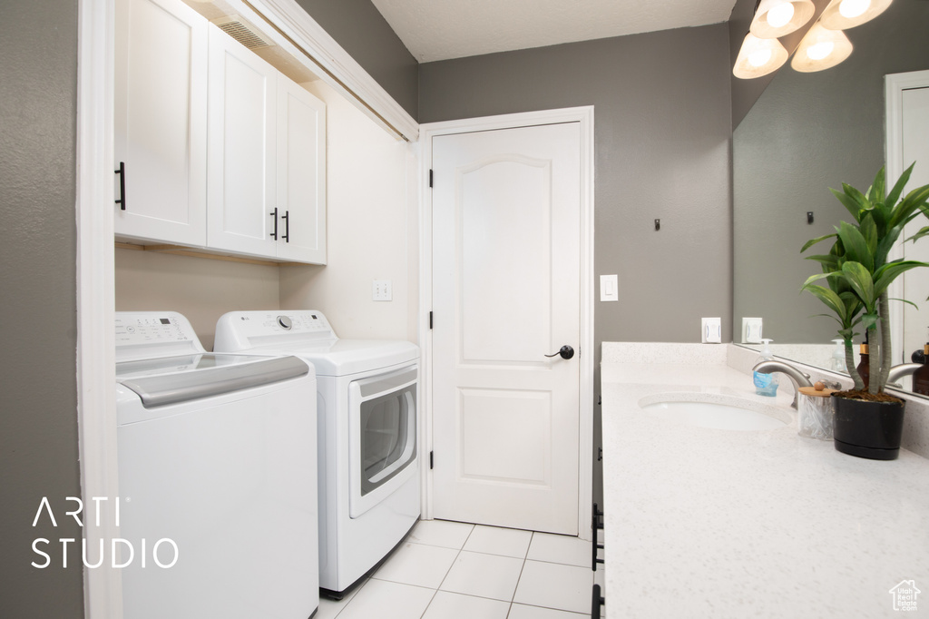 Clothes washing area with sink, washing machine and dryer, light tile floors, and cabinets