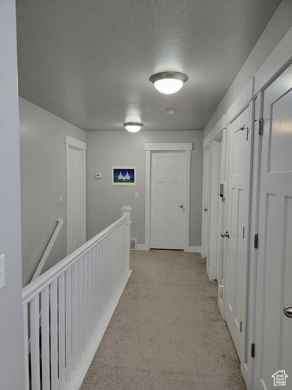 Corridor featuring a textured ceiling and light carpet