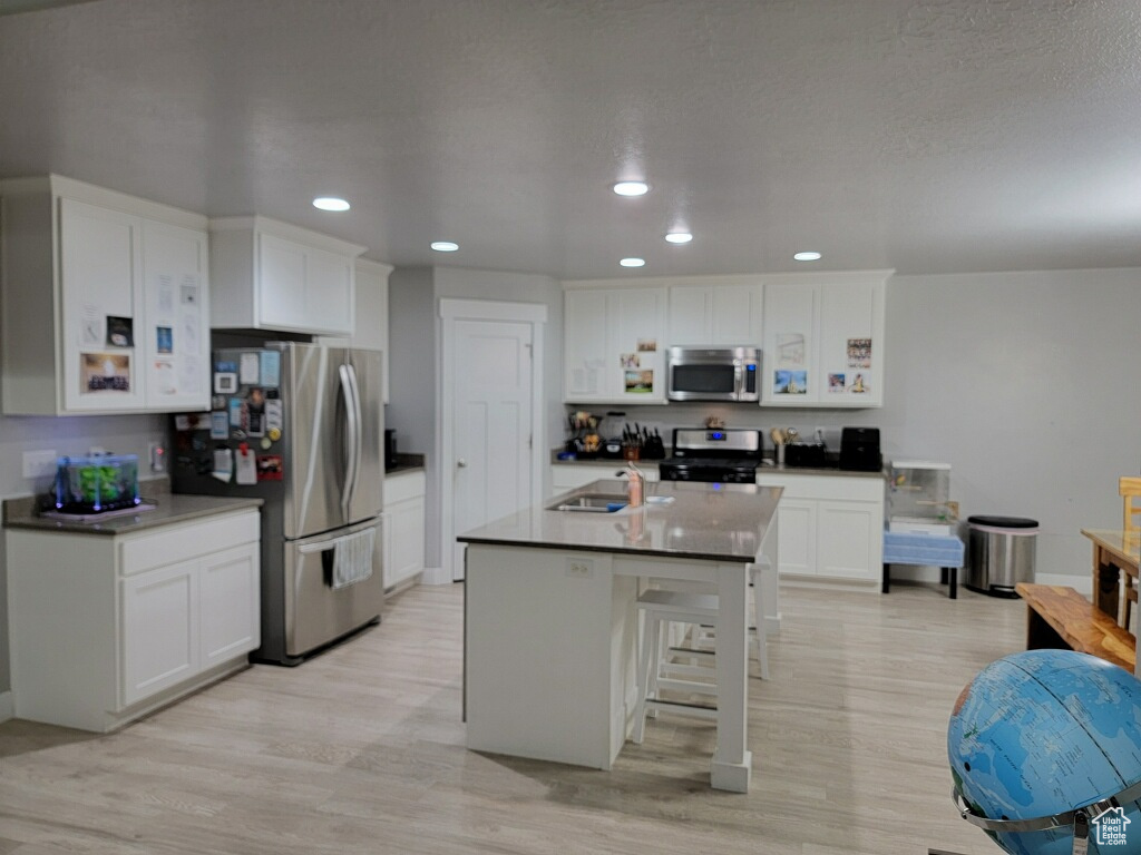 Kitchen with a kitchen bar, light hardwood / wood-style flooring, stainless steel appliances, white cabinets, and sink