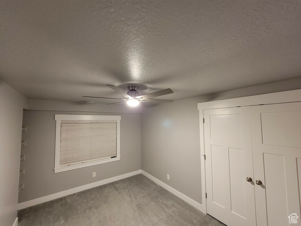 Empty room with ceiling fan, dark carpet, and a textured ceiling