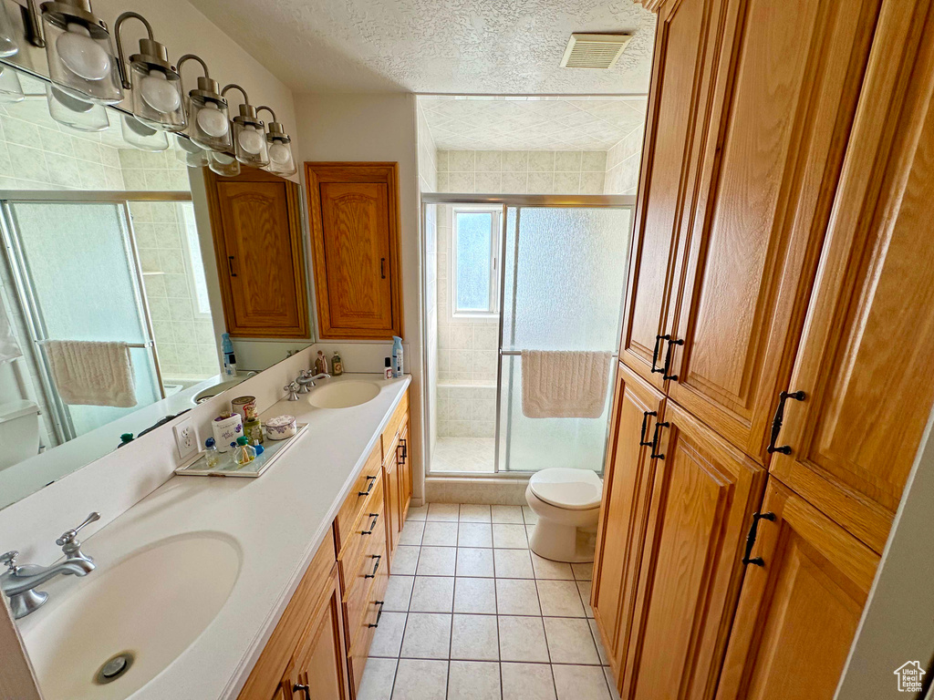 Bathroom featuring a shower with shower door, toilet, double vanity, tile flooring, and a textured ceiling