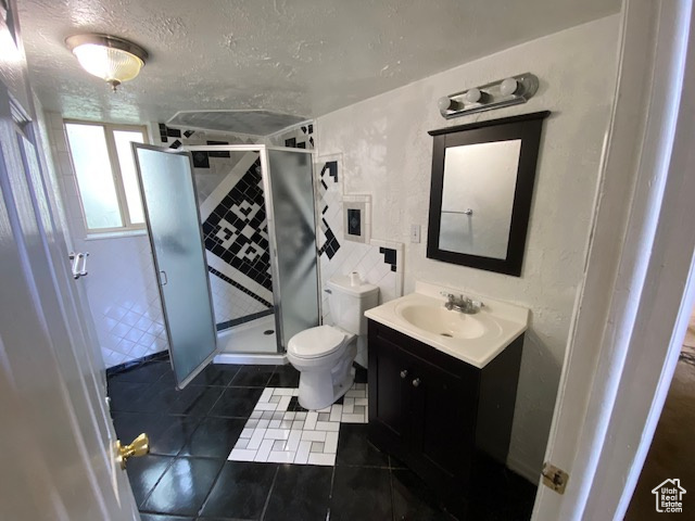 Bathroom featuring vanity with extensive cabinet space, toilet, a textured ceiling, an enclosed shower, and tile floors