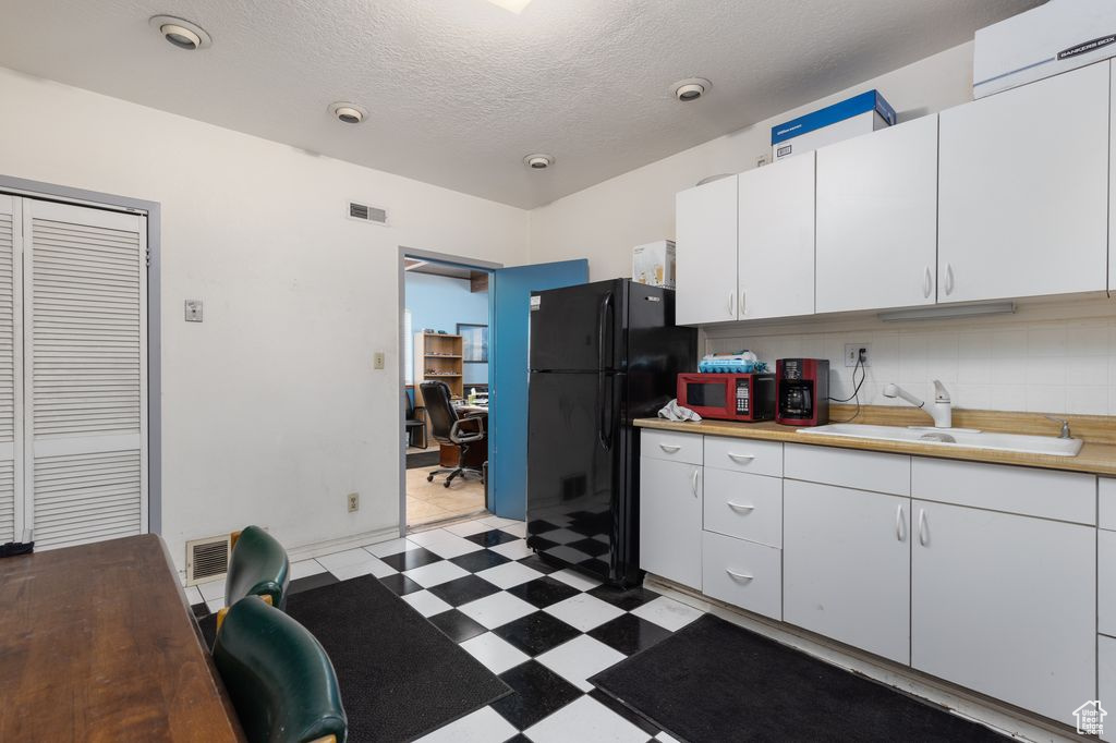 Kitchen with light tile floors, sink, backsplash, white cabinetry, and black appliances