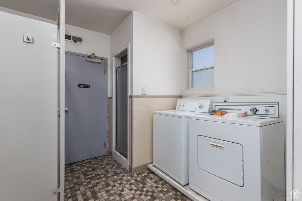 Washroom with tile walls, tile floors, and washer and clothes dryer