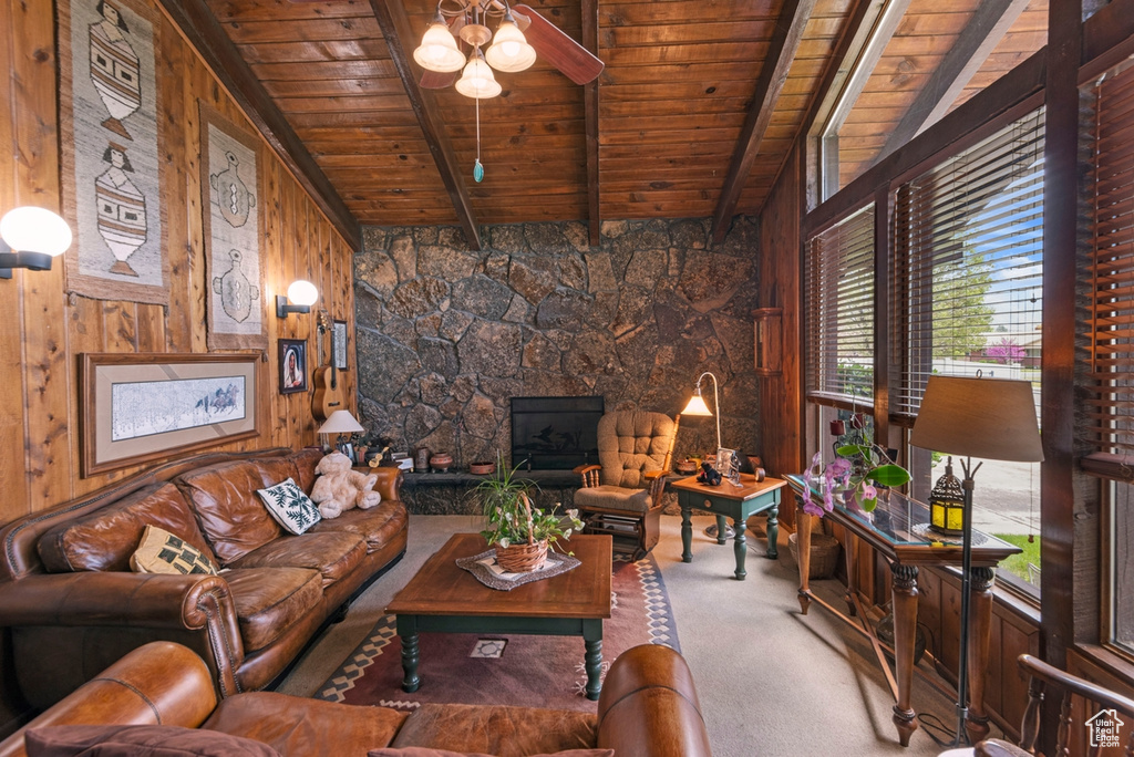 Carpeted living room with wood walls, ceiling fan, lofted ceiling with beams, wooden ceiling, and a fireplace