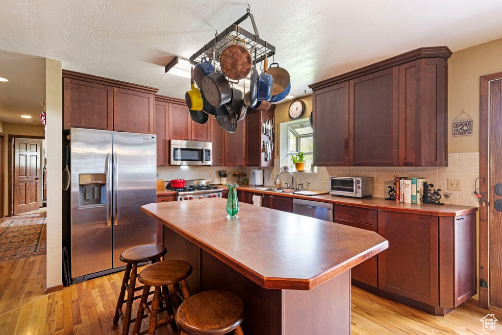 Kitchen featuring light hardwood / wood-style flooring, backsplash, a center island, and stainless steel appliances