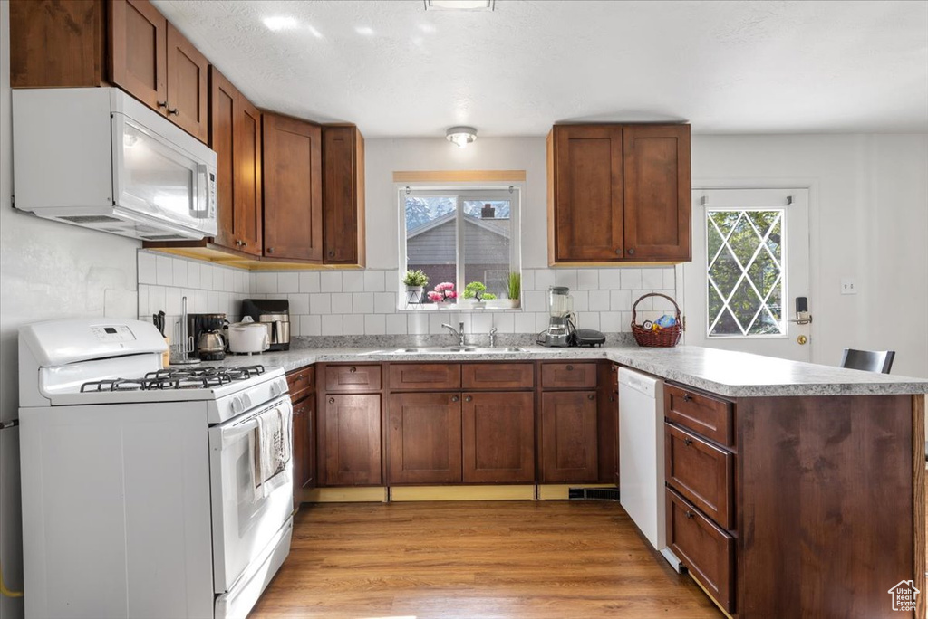 Kitchen with white appliances, light hardwood / wood-style flooring, backsplash, kitchen peninsula, and sink