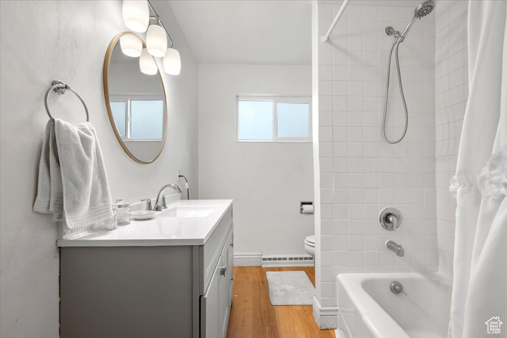 Full bathroom with shower / bath combo, toilet, wood-type flooring, vanity, and baseboard heating