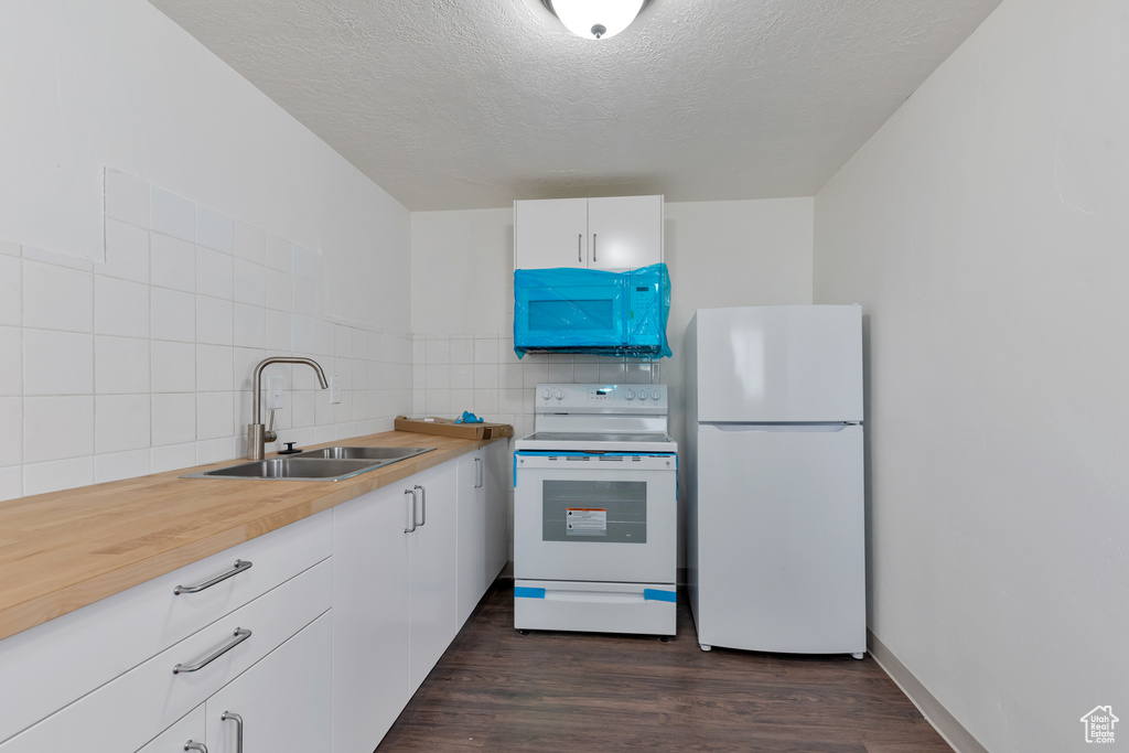 Kitchen with a textured ceiling, sink, white appliances, backsplash, and dark hardwood / wood-style flooring