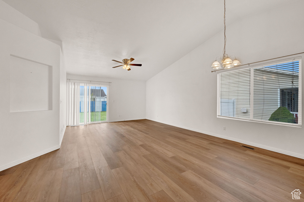 Spare room featuring high vaulted ceiling, light hardwood / wood-style floors, and ceiling fan with notable chandelier
