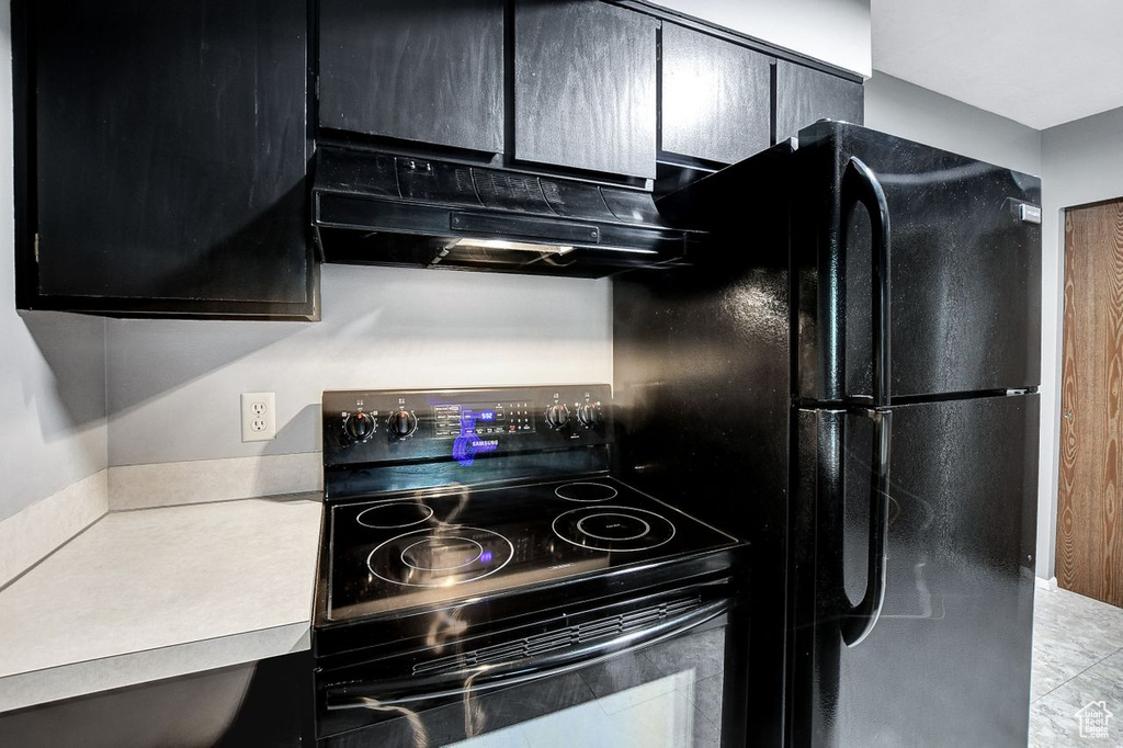 Kitchen with custom exhaust hood, black fridge, light tile floors, and range