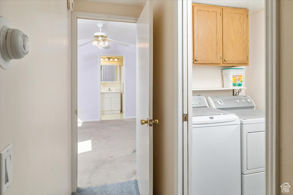 Clothes washing area with light colored carpet, cabinets, ceiling fan, and washer and clothes dryer