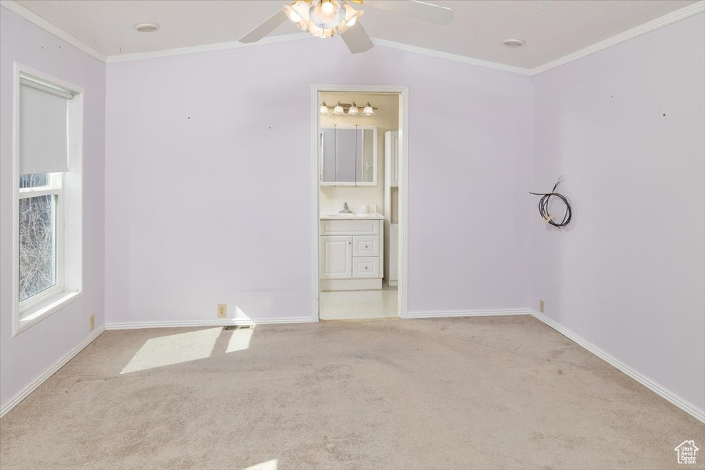 Unfurnished bedroom featuring ceiling fan, ensuite bathroom, light carpet, and ornamental molding