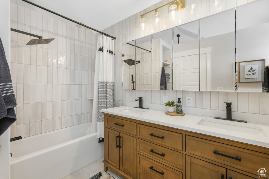 Bathroom featuring tile flooring, tile walls, shower / bath combo with shower curtain, tasteful backsplash, and dual bowl vanity