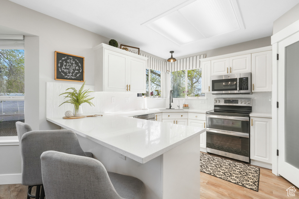 Kitchen with a wealth of natural light, light hardwood / wood-style floors, stainless steel appliances, and white cabinets